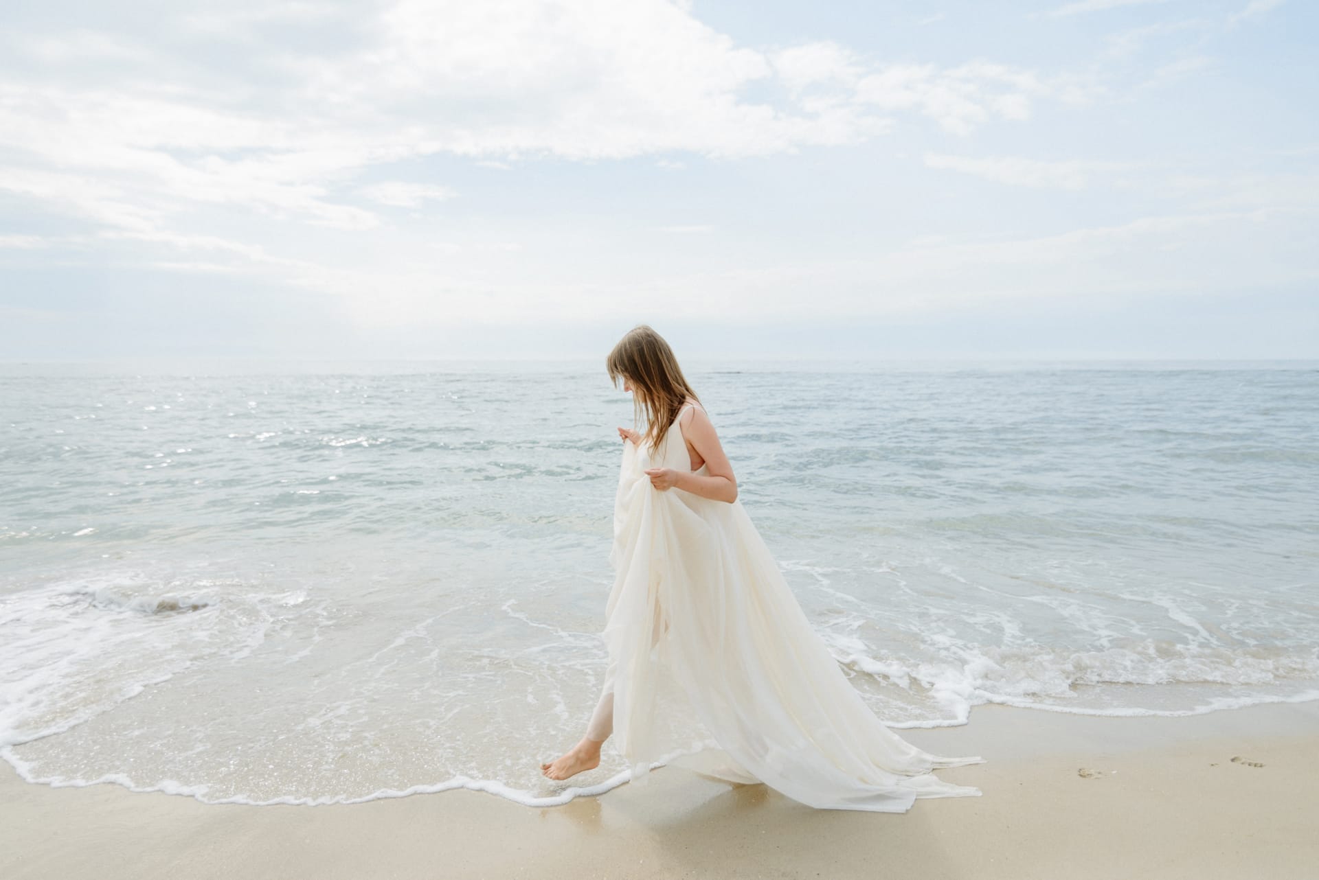Woman long white dress walks along beach pier against sea