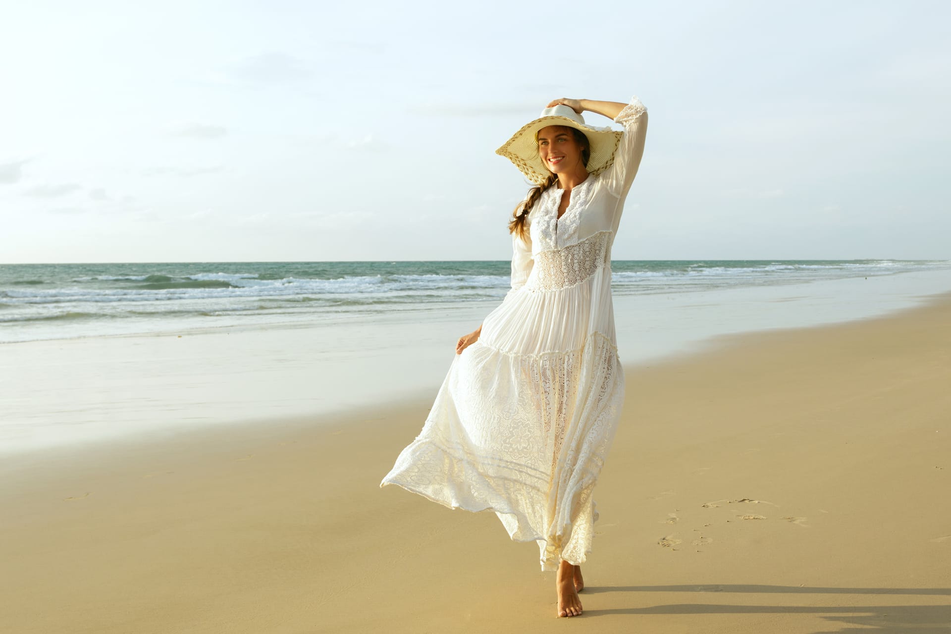 Woman wearing beautiful white dress is walking beach during sunset image