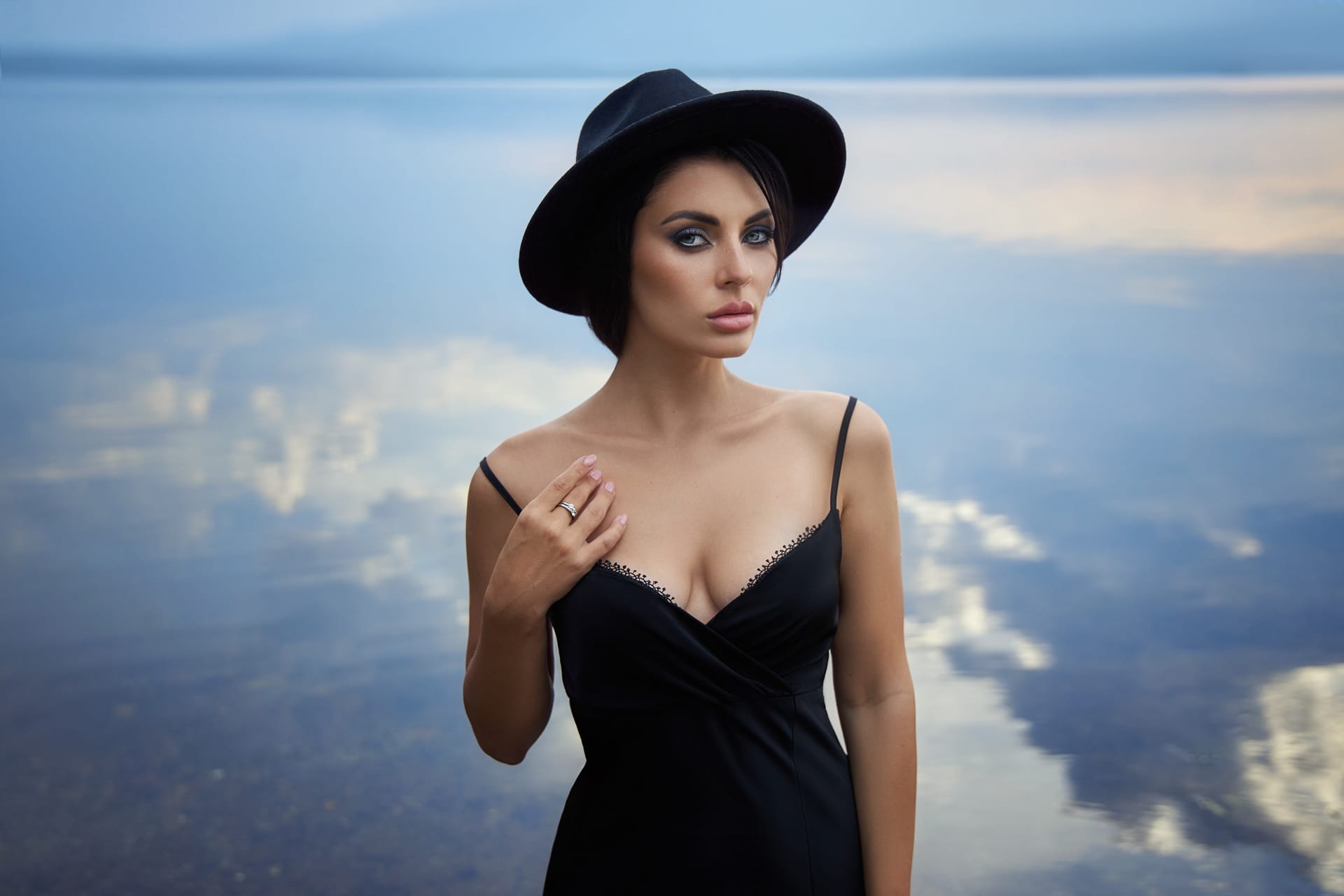 Beauty woman black hat black dress poses near lake against blue sky image