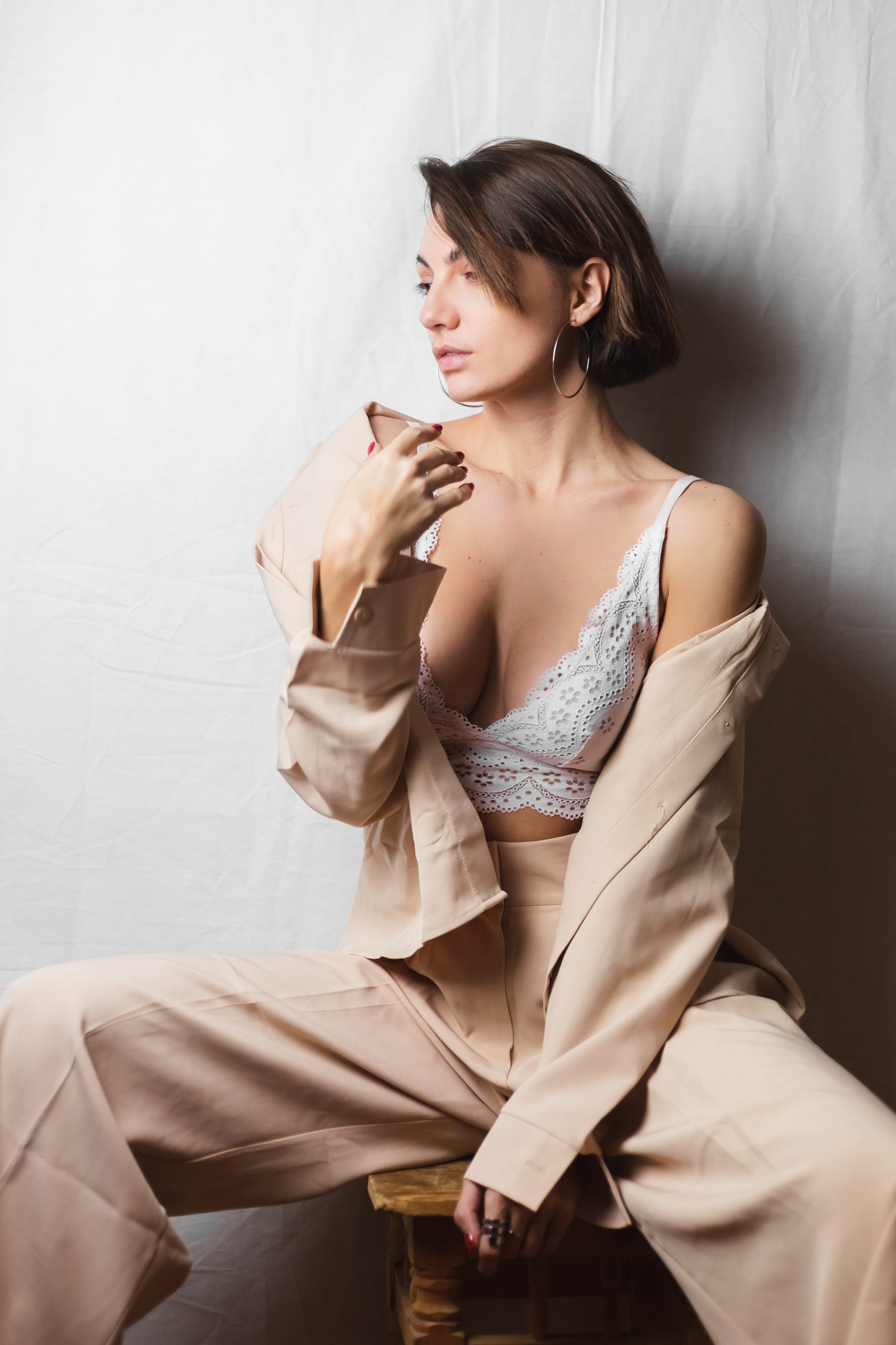 Woman with big breasts beige suit white lace bra sits chair gray white