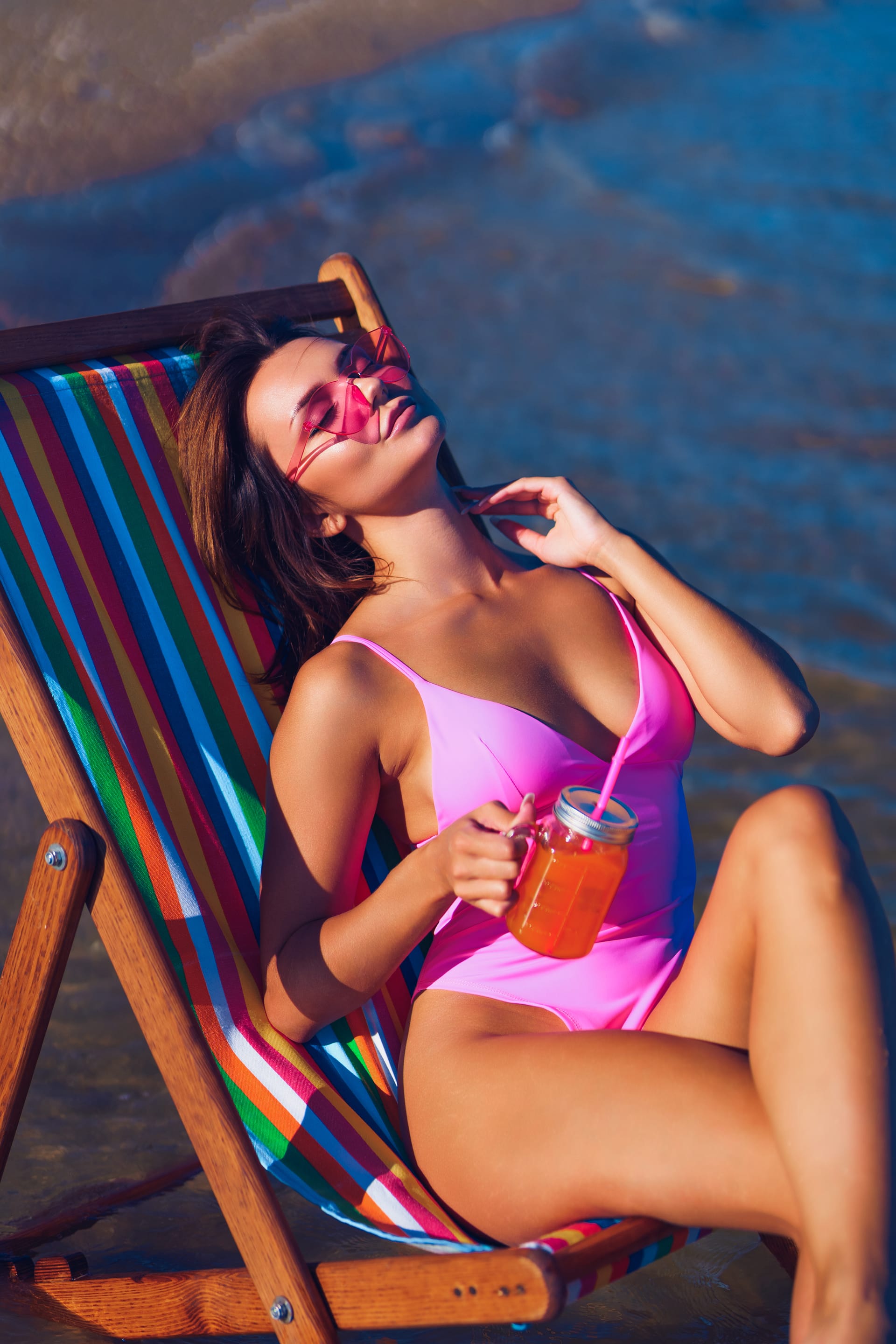 Attractive redhead girl deckchair sunbathing near sea with glass juice her hand