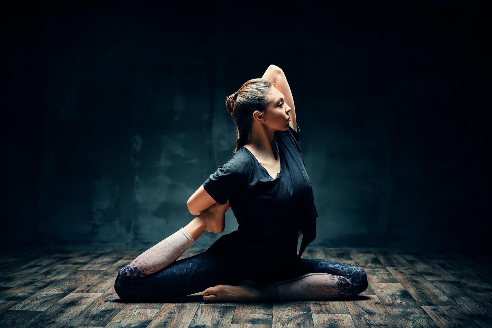 Practicing yoga doing one legged king pigeon pose dark room