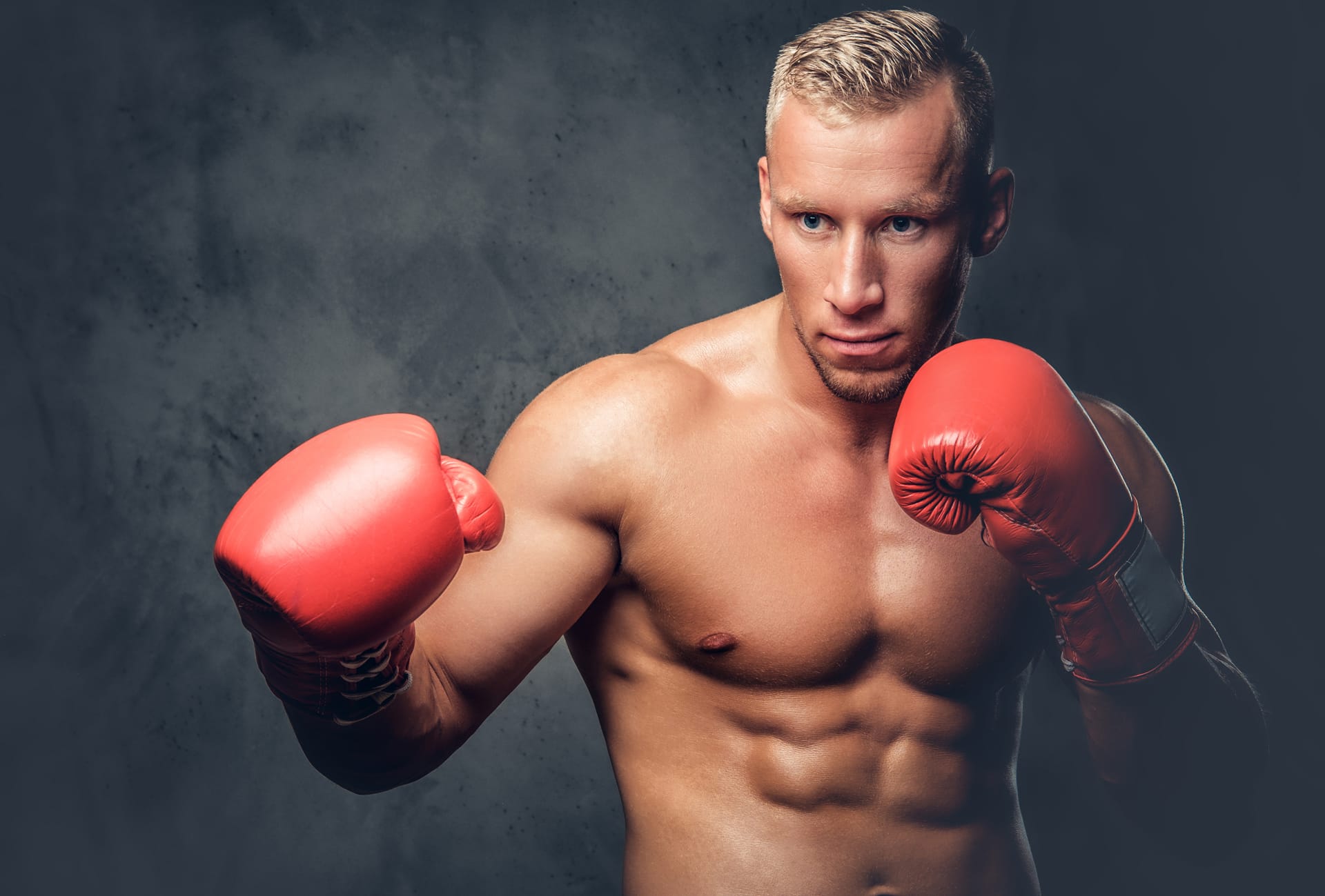 Shirtless kick boxer showing his punches kicks grey background studio