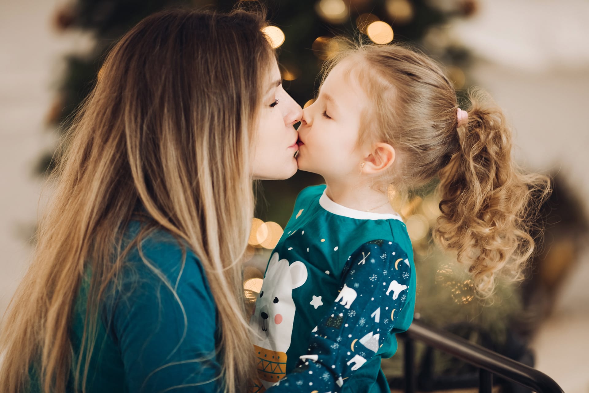 Up photo brunette lady kissing little girl with christmas tree holiday concept
