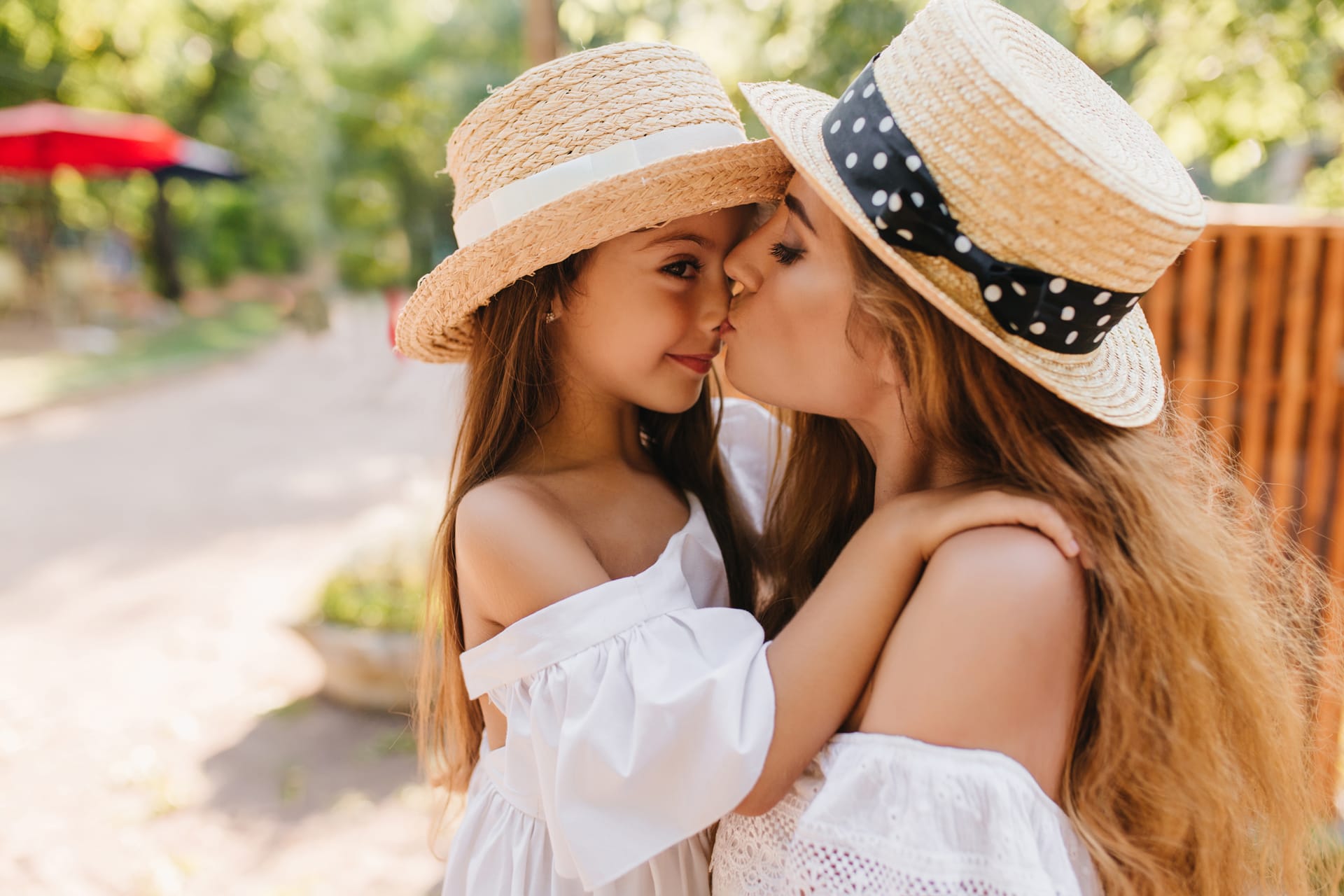 Young woman standing beside wooden fence kissing her little daughter with love