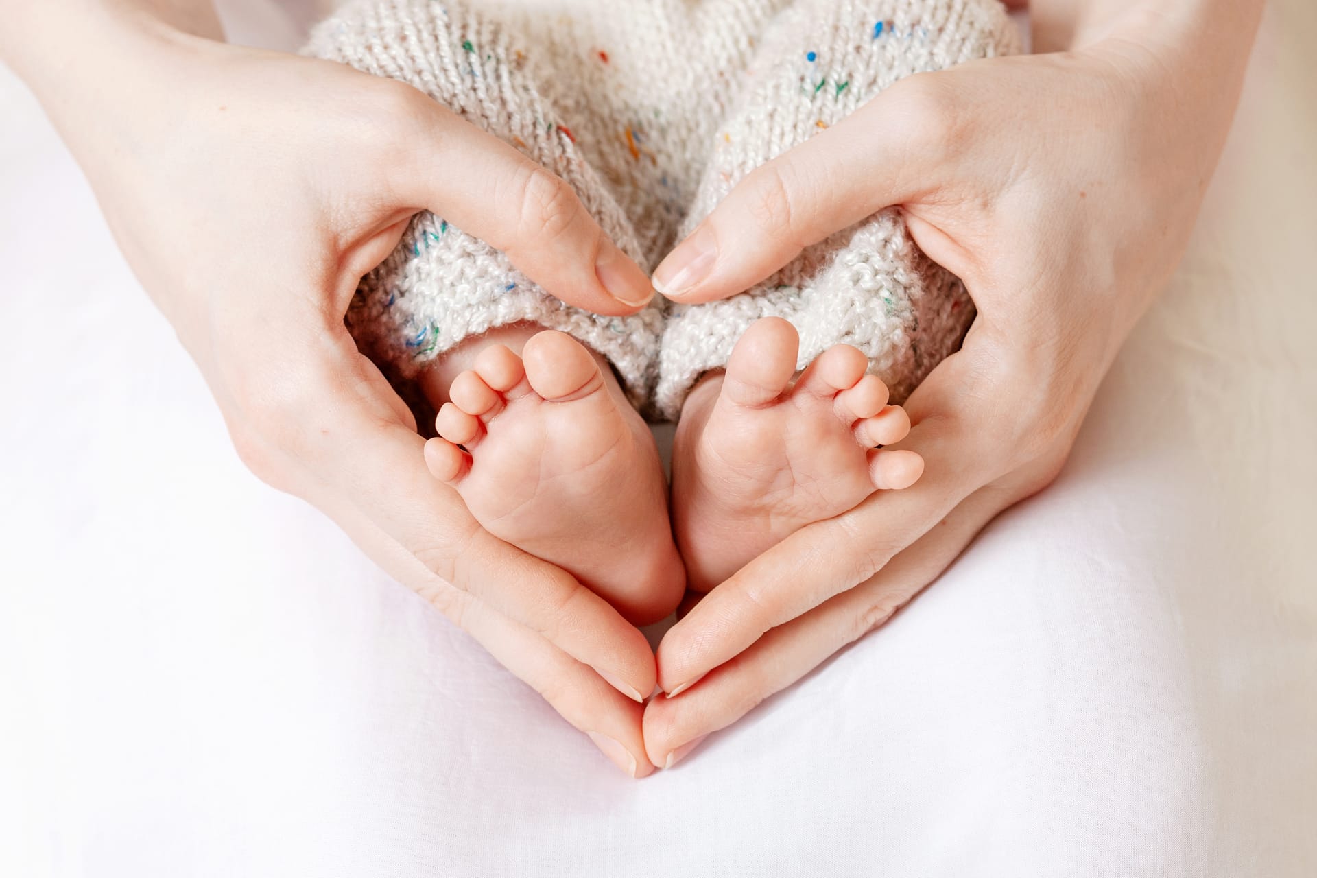 Mother hands tiny newborn baby s feet female heart shaped hands closeup