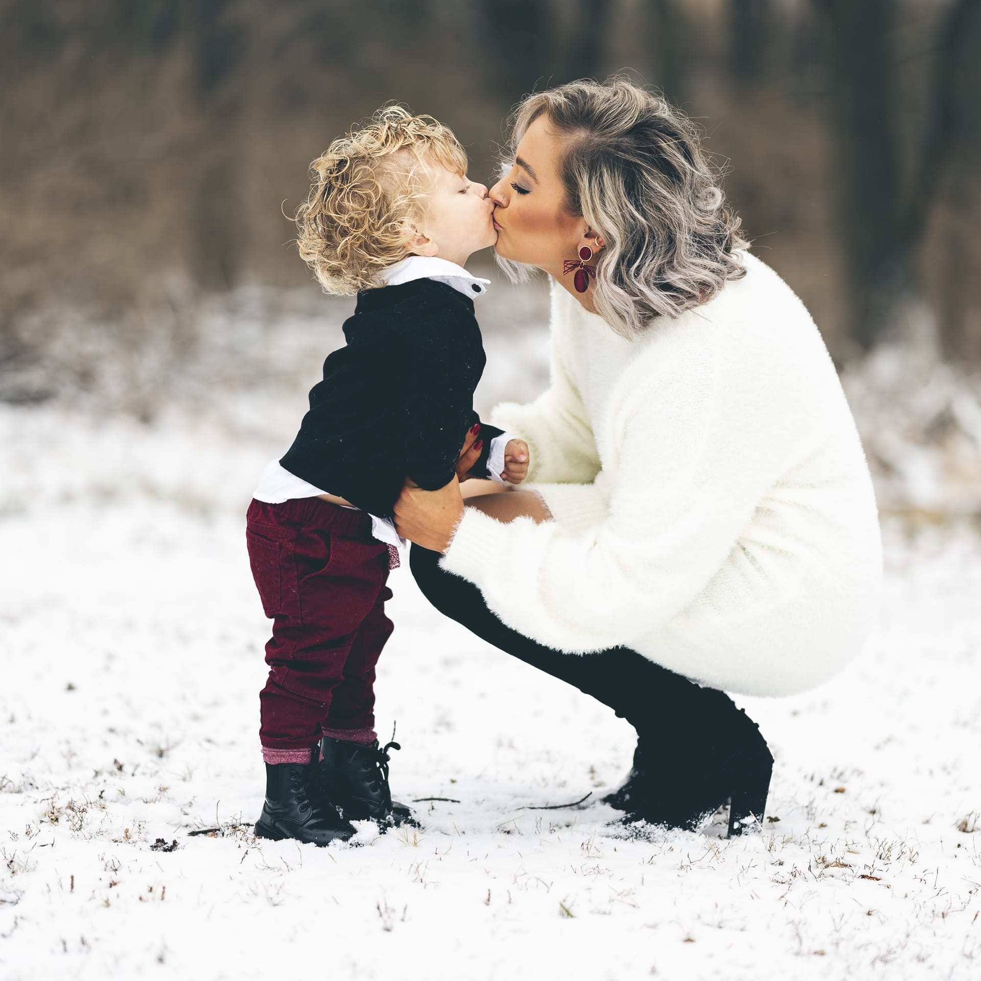 Young mother giving her son kiss lips outdoors winter day
