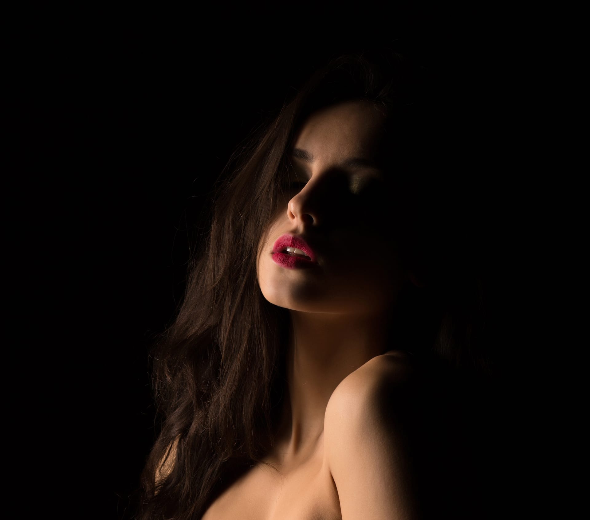 Sensual brunette young woman with naked shoulders posing dark studio