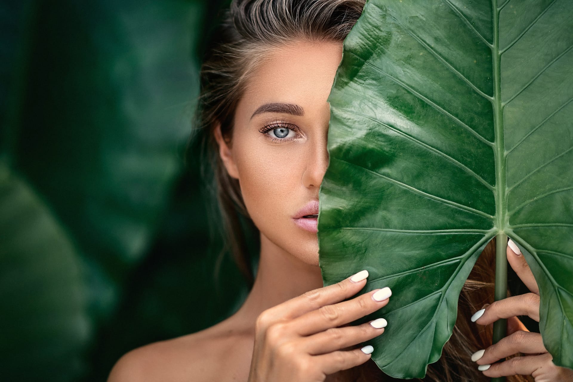 Beautiful young woman with natural makeup holds big green leaf blurred green
