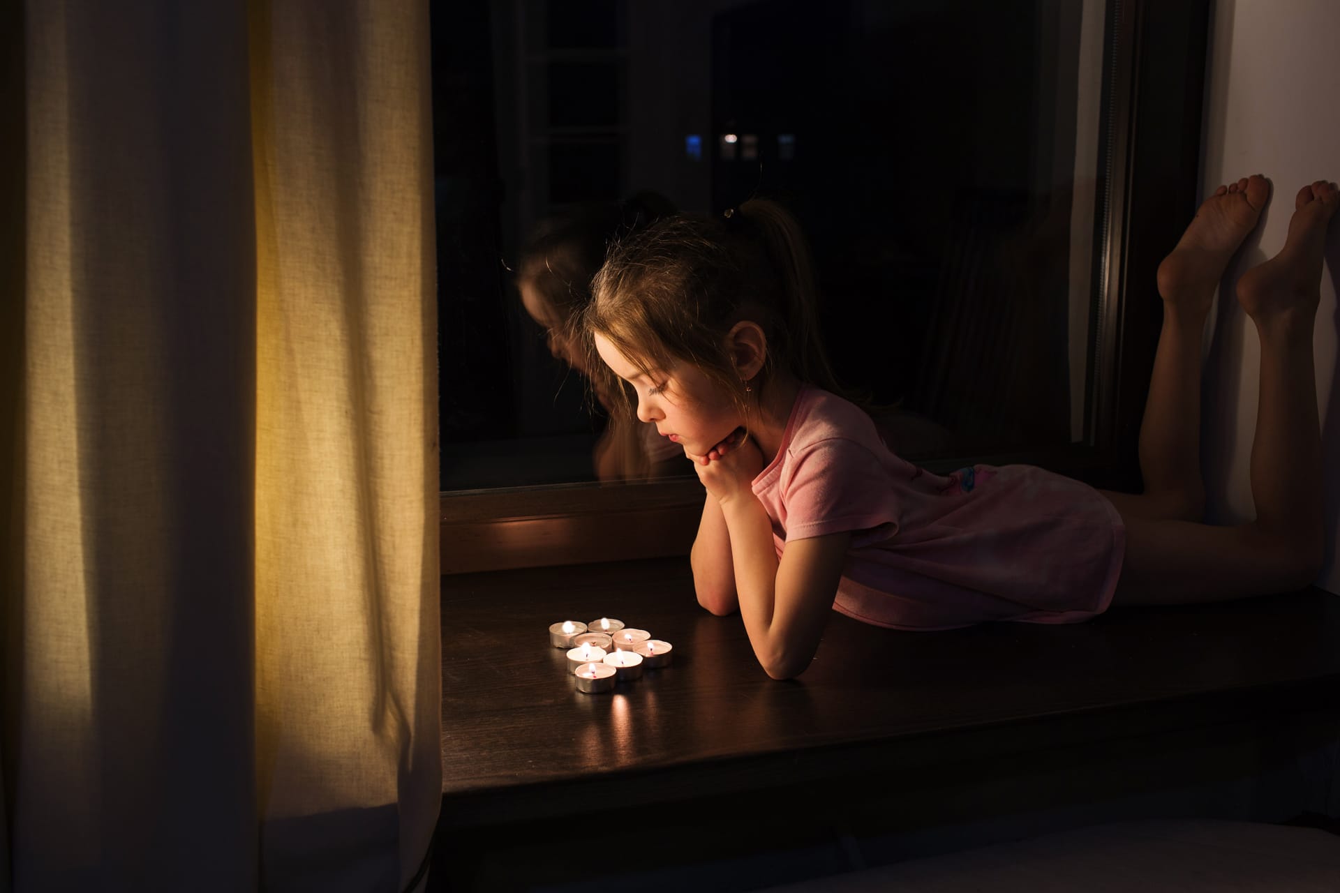 Little girl tshirt lies windowsill near window looks burning candles