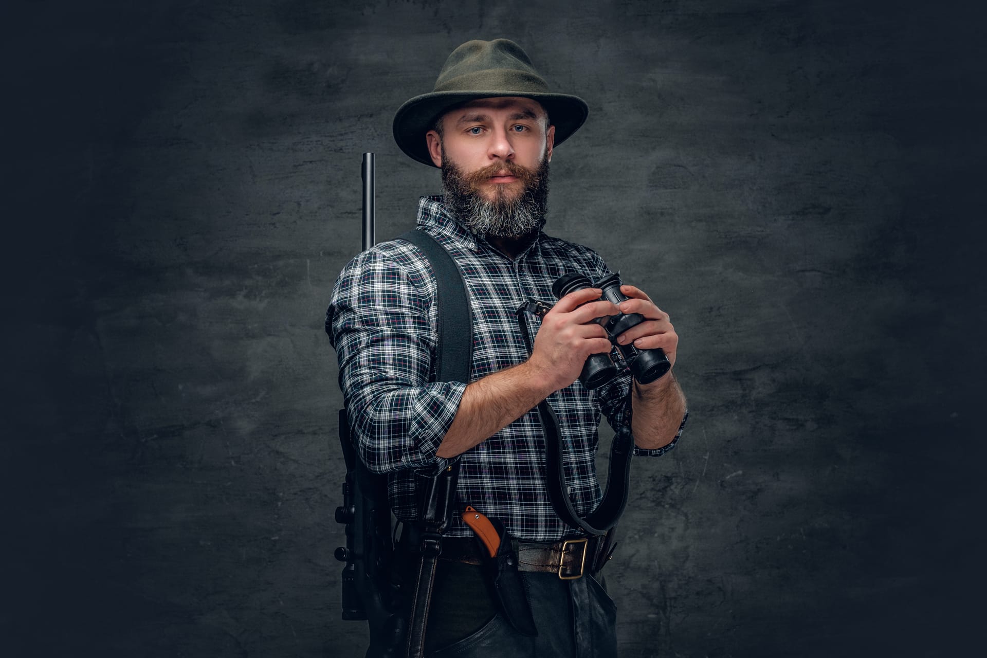 Studio portrait bearded hunter holds rifle binocular