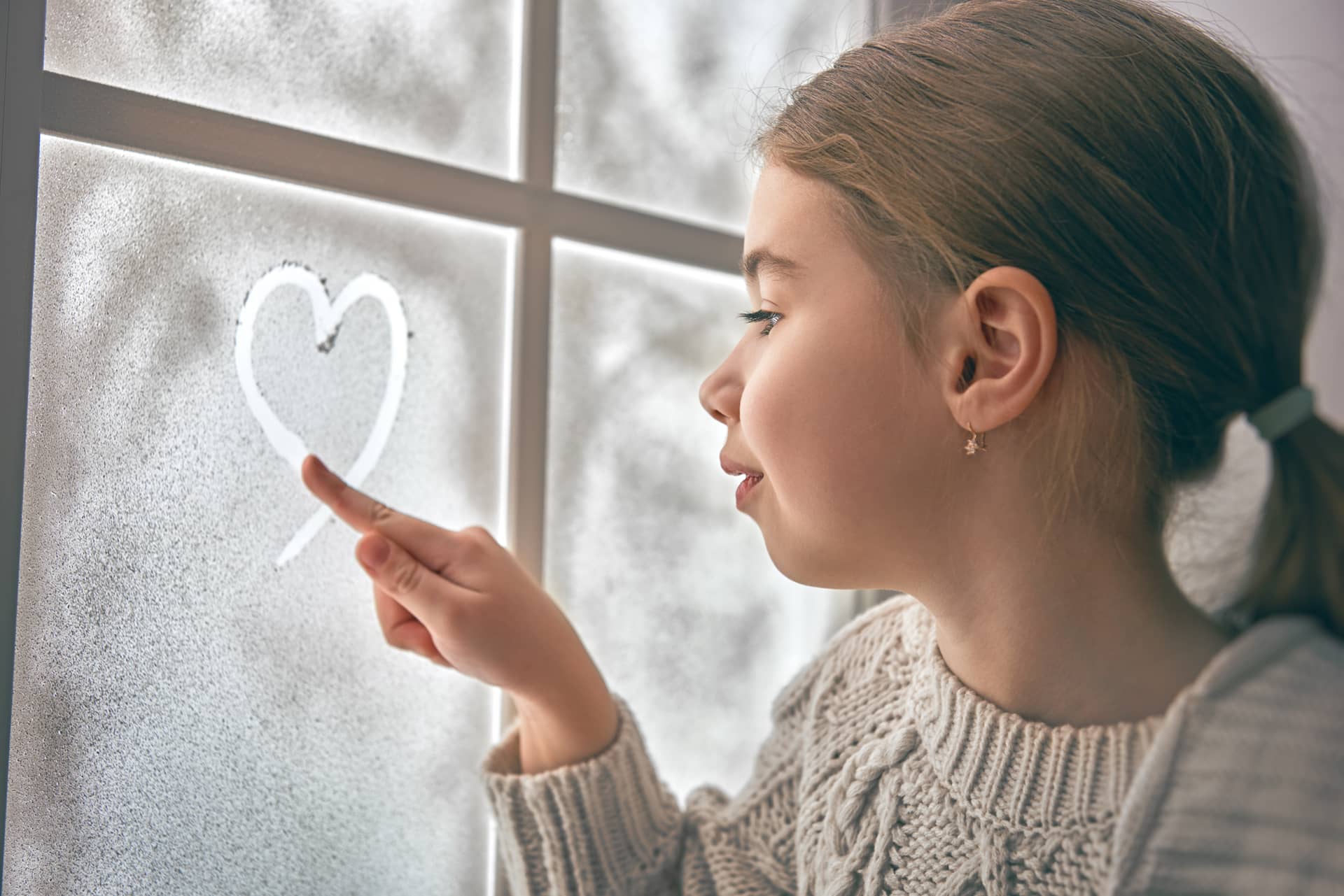 Sitting by window drawing heart frozen glass kid enjoys winter
