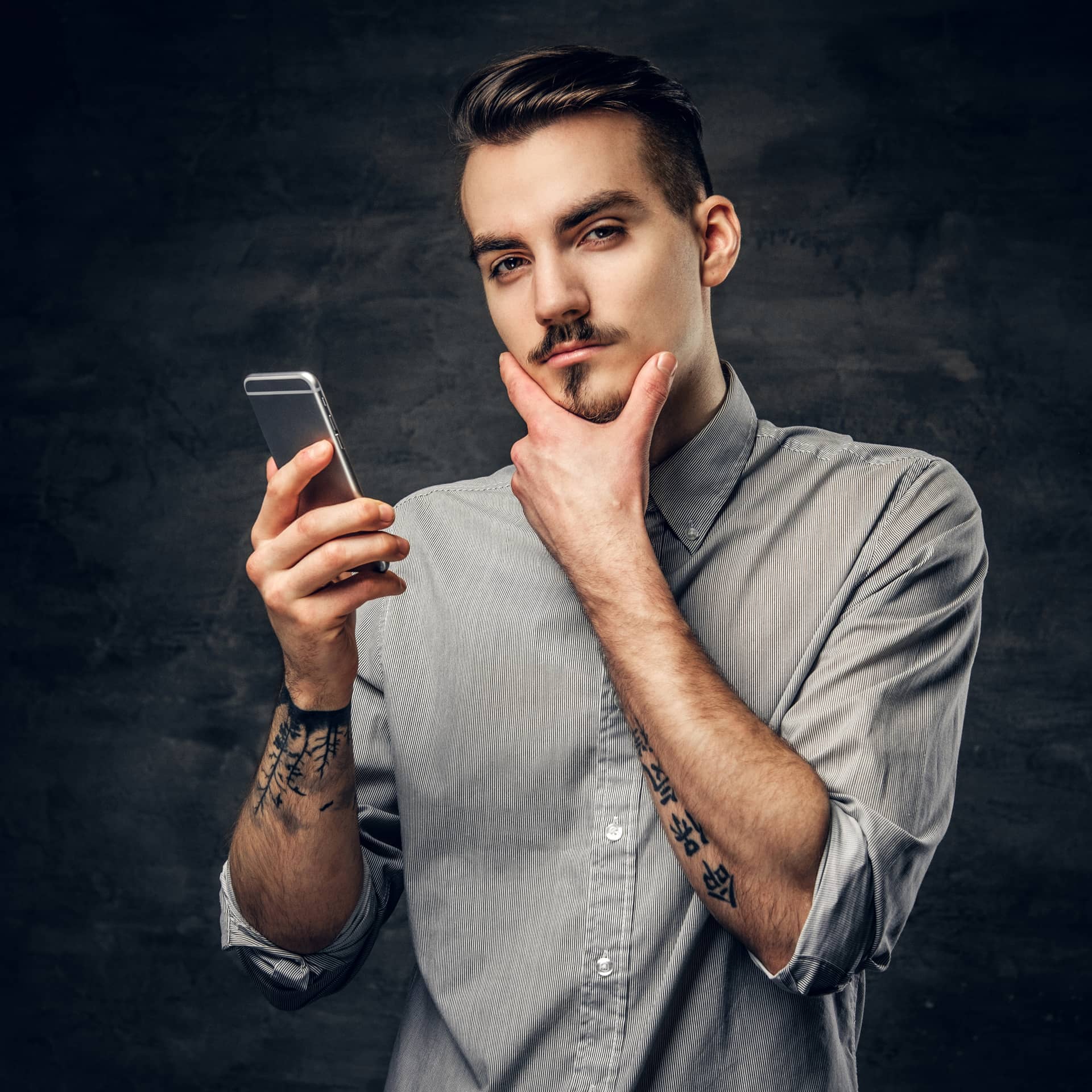 Handsome bearded hipster male with tattoo his arm using smartphone