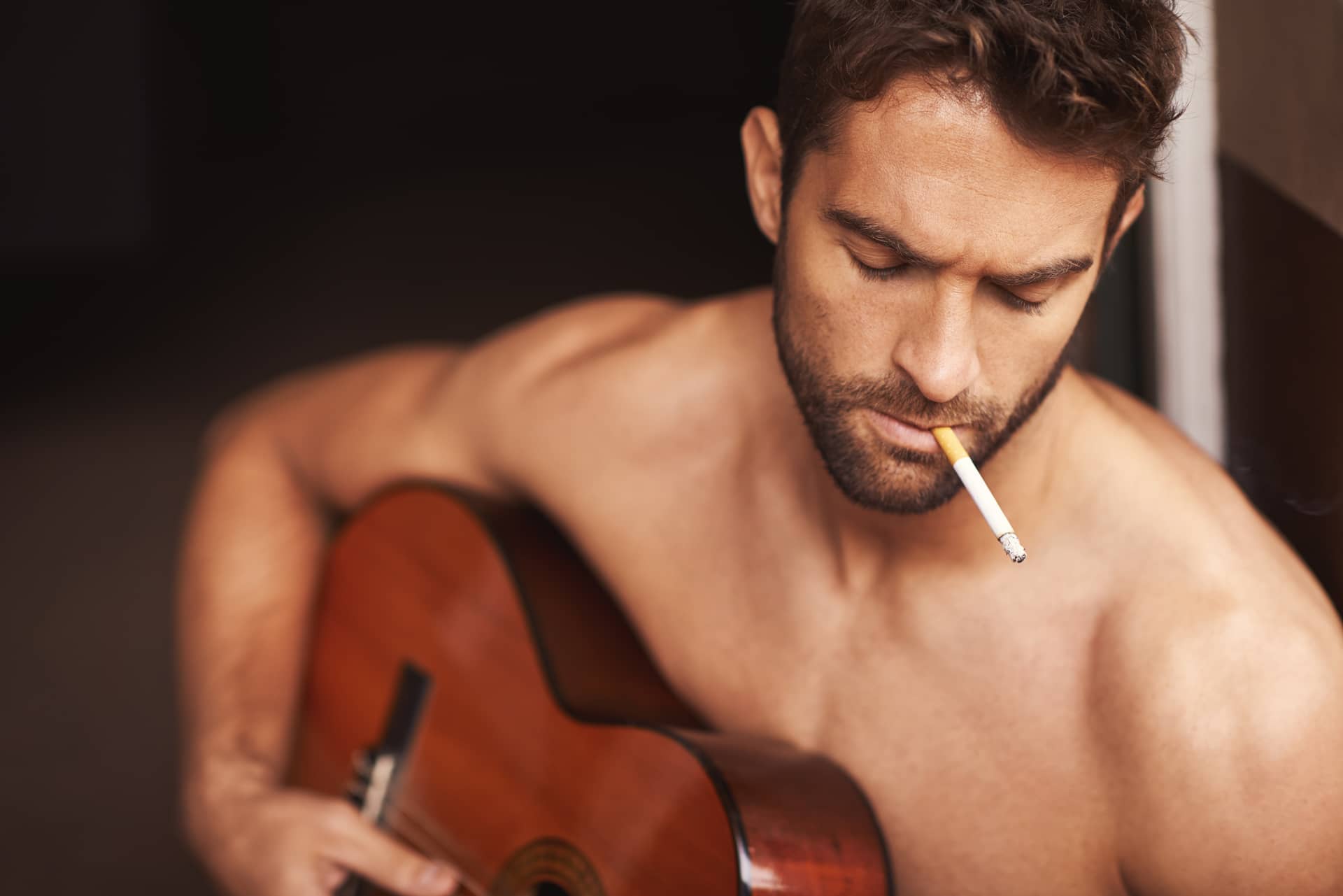 Latest song cropped shot shirtless young man playing guitar home