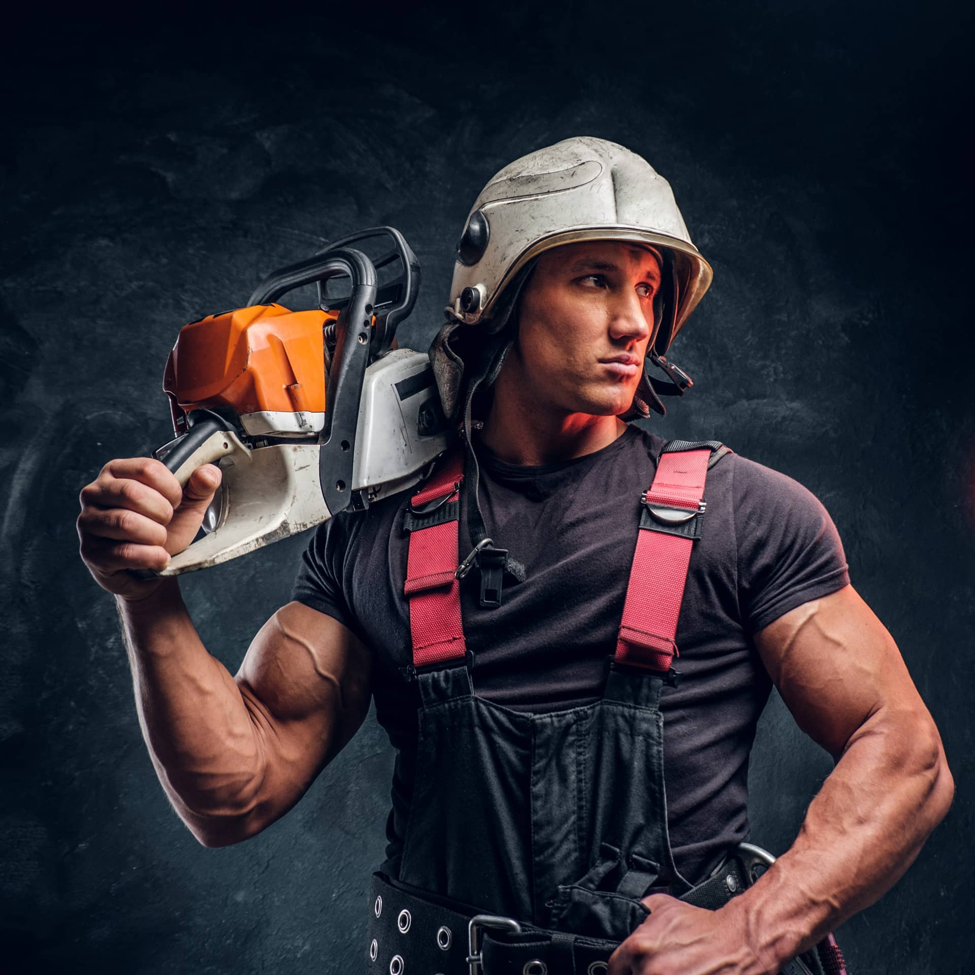 Wearing protective clothes posing with chainsaw looks sideways dark studio