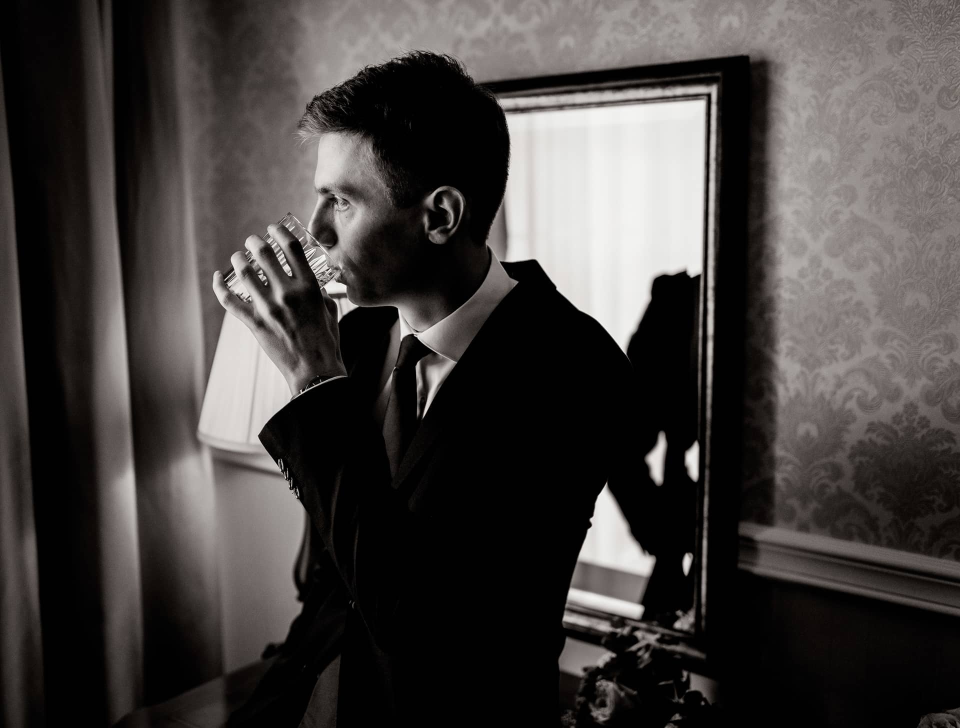 Monochrome portrait handsome young man room is drinking dressed suit