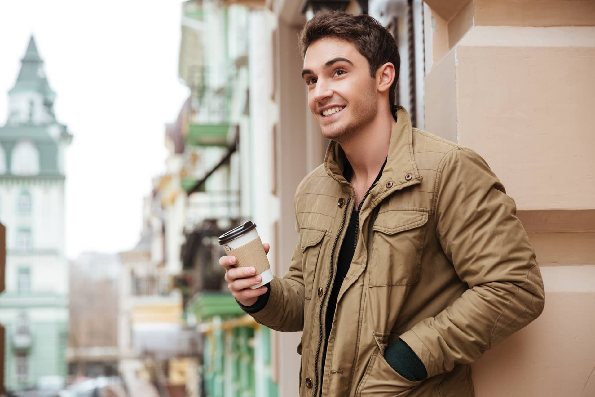 Young man walking street looking aside while holding cup coffee