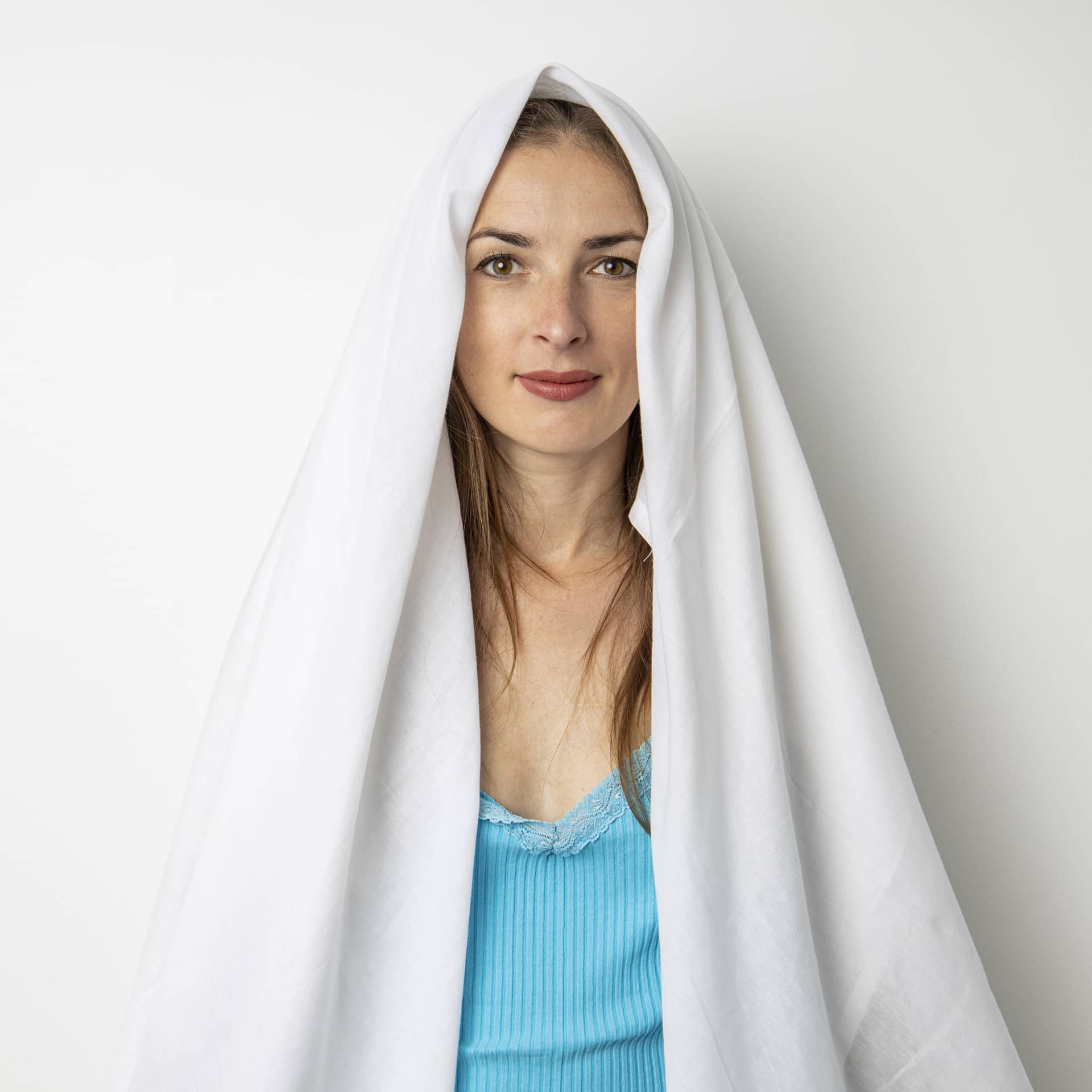Smiling young woman covering her head with sheet white background