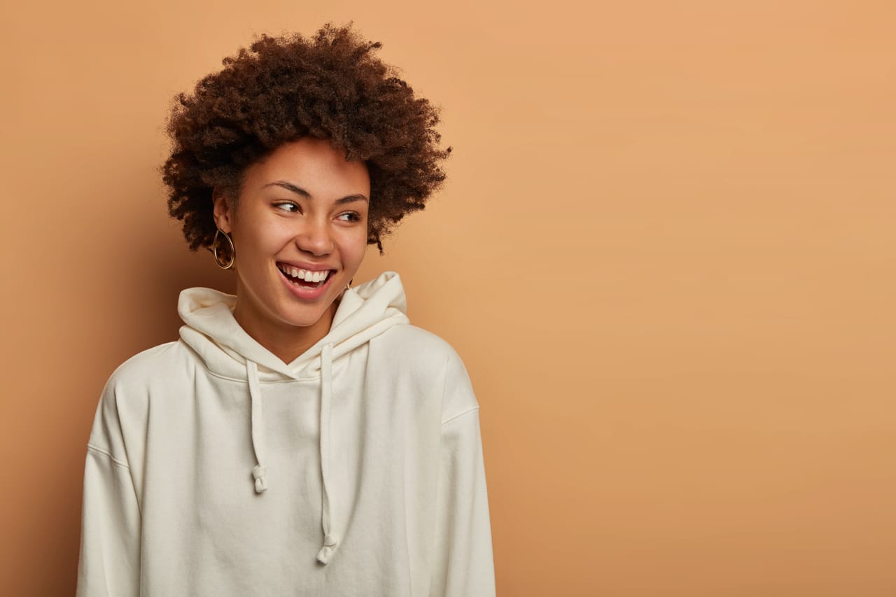 Related image emotions lifestyle concept happy delighted dark skinned curly woman wears white sweatshirt laughs has fun looks aside