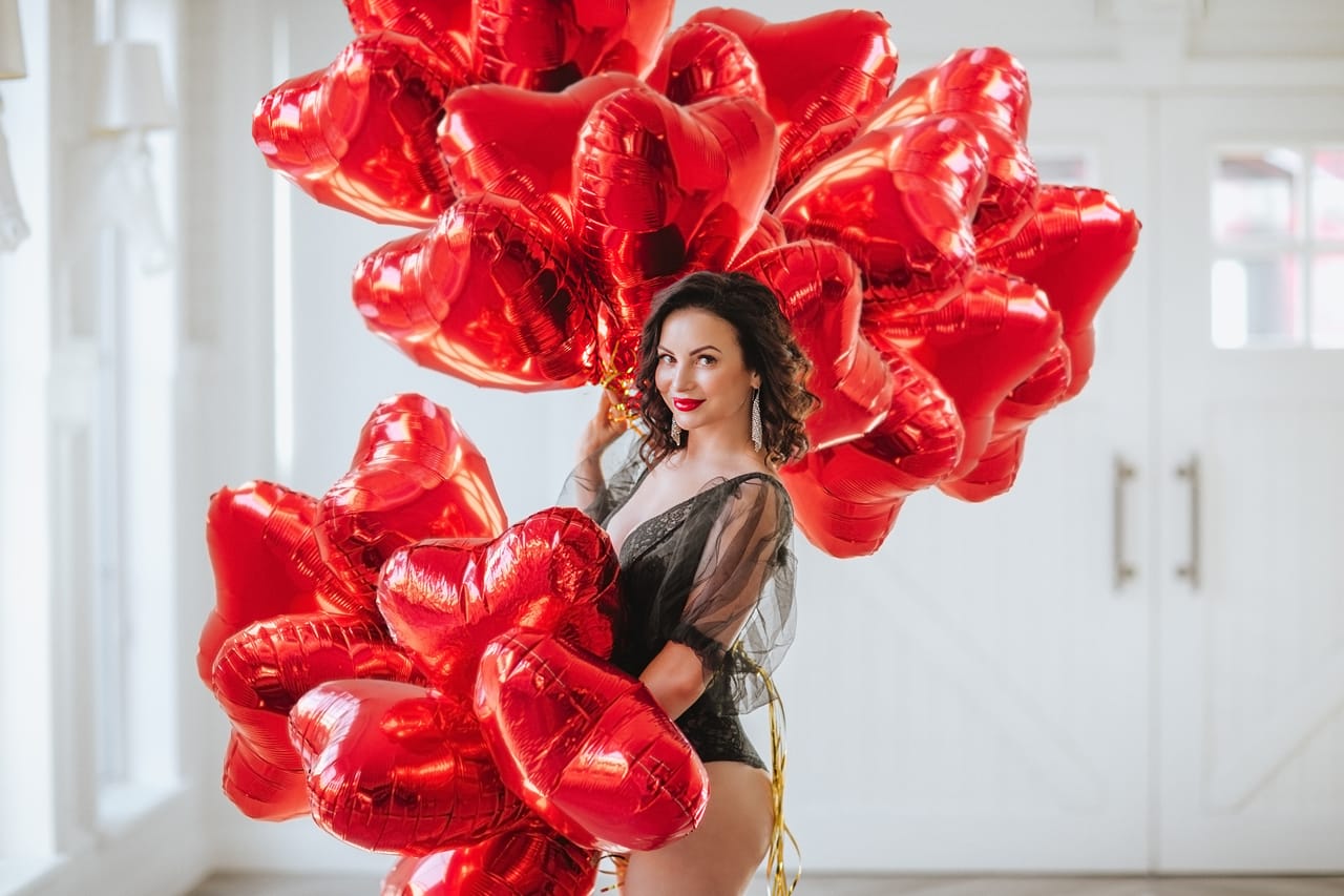 Related image pretty brunette woman black body posing with bunch red balloons like hearts against white background