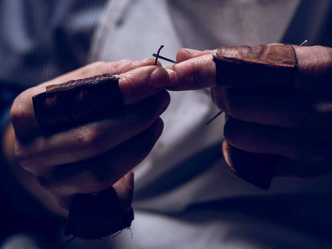 Related image crop craftsman placing thread into needle sewing leather fabric
