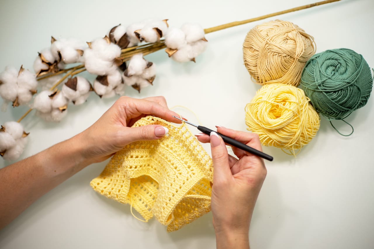 Related image womans hands are knitting baby clothes from yellow yarn white table top view